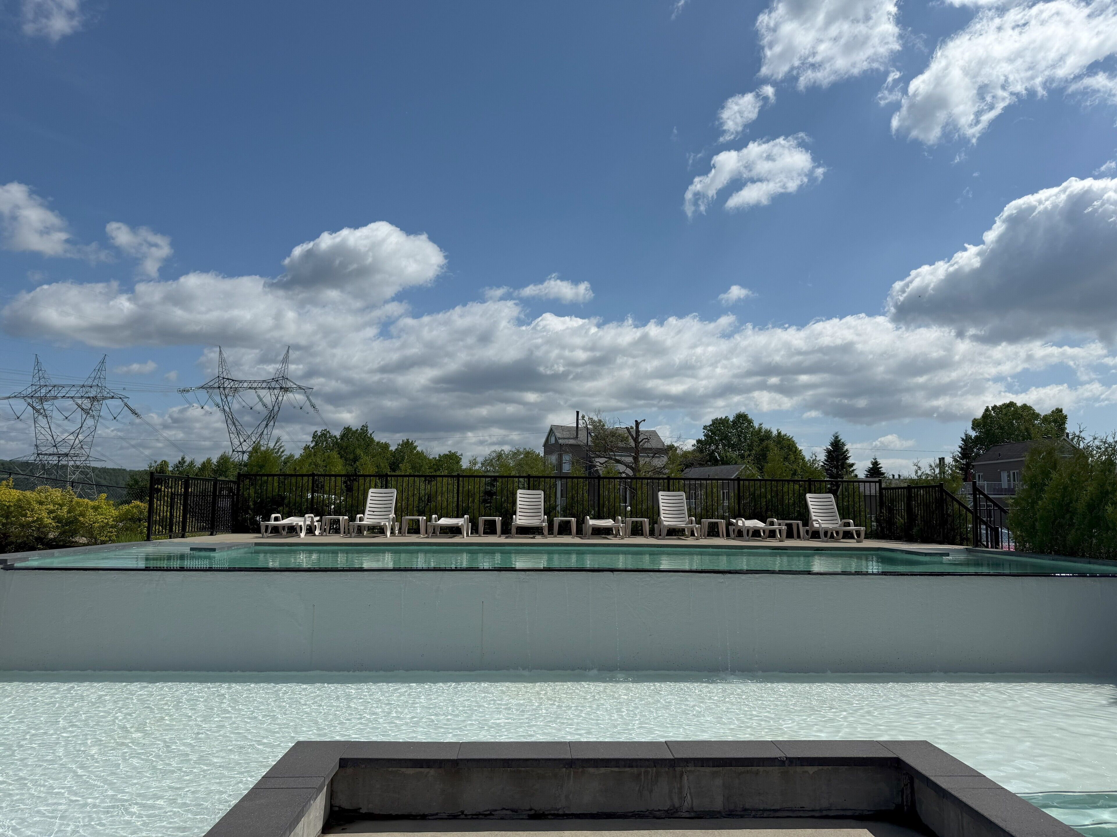 Una piscina con sillas de descanso y vistas al cielo y árboles.