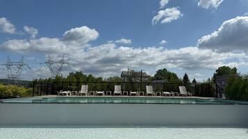 Una piscina con sillas de descanso y vistas al cielo y árboles.