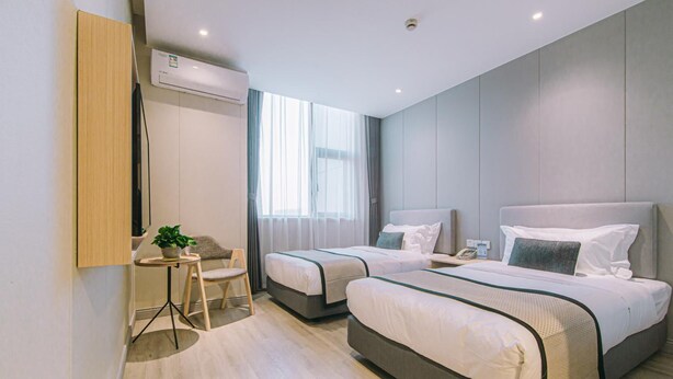 Una habitación de hotel moderna con dos camas, un escritorio pequeño, una silla y una planta en maceta.