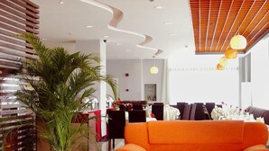Un moderno vestíbulo de hotel con un sofá naranja grande, una mesa de centro de vidrio y una planta en maceta.