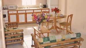 Une cuisine avec des meubles de rangement en bois, un four à micro-ondes, une machine à café et un réfrigérateur. On y trouve une table à manger avec des chaises et un vase rempli de fleurs.