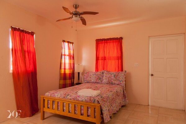Un dormitorio con una cama de madera, cortinas rojas, un ventilador de techo y una puerta blanca.
