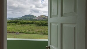 Une vue à travers une porte ouverte, donnant sur un champ verdoyant avec des collines à l’horizon.