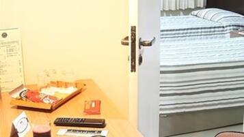 A hotel room with a wooden desk, a bed with striped bedding, and a door leading to another room.