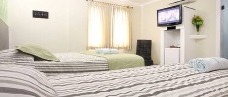 Habitación de hotel con dos camas, televisión, escritorio pequeño y ventana con cortinas.