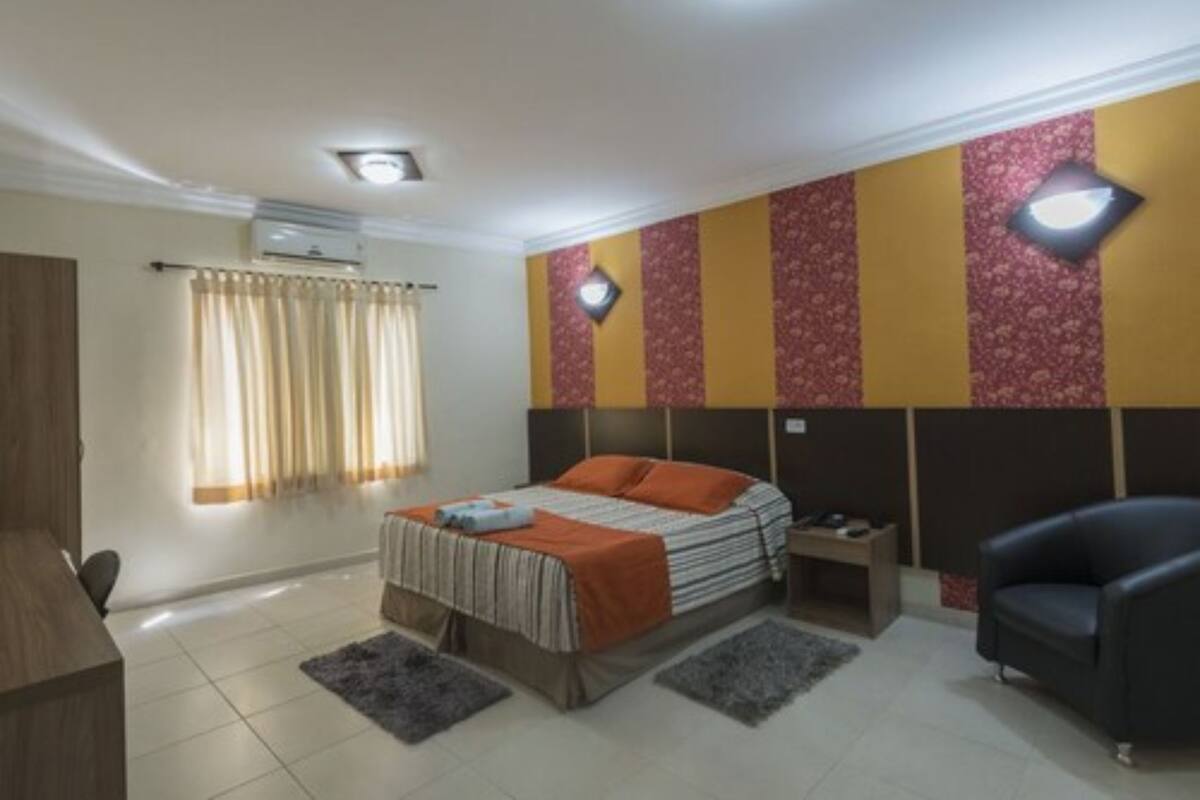 A bedroom with a bed, bedside tables, a chair, and a wall-mounted light fixture.