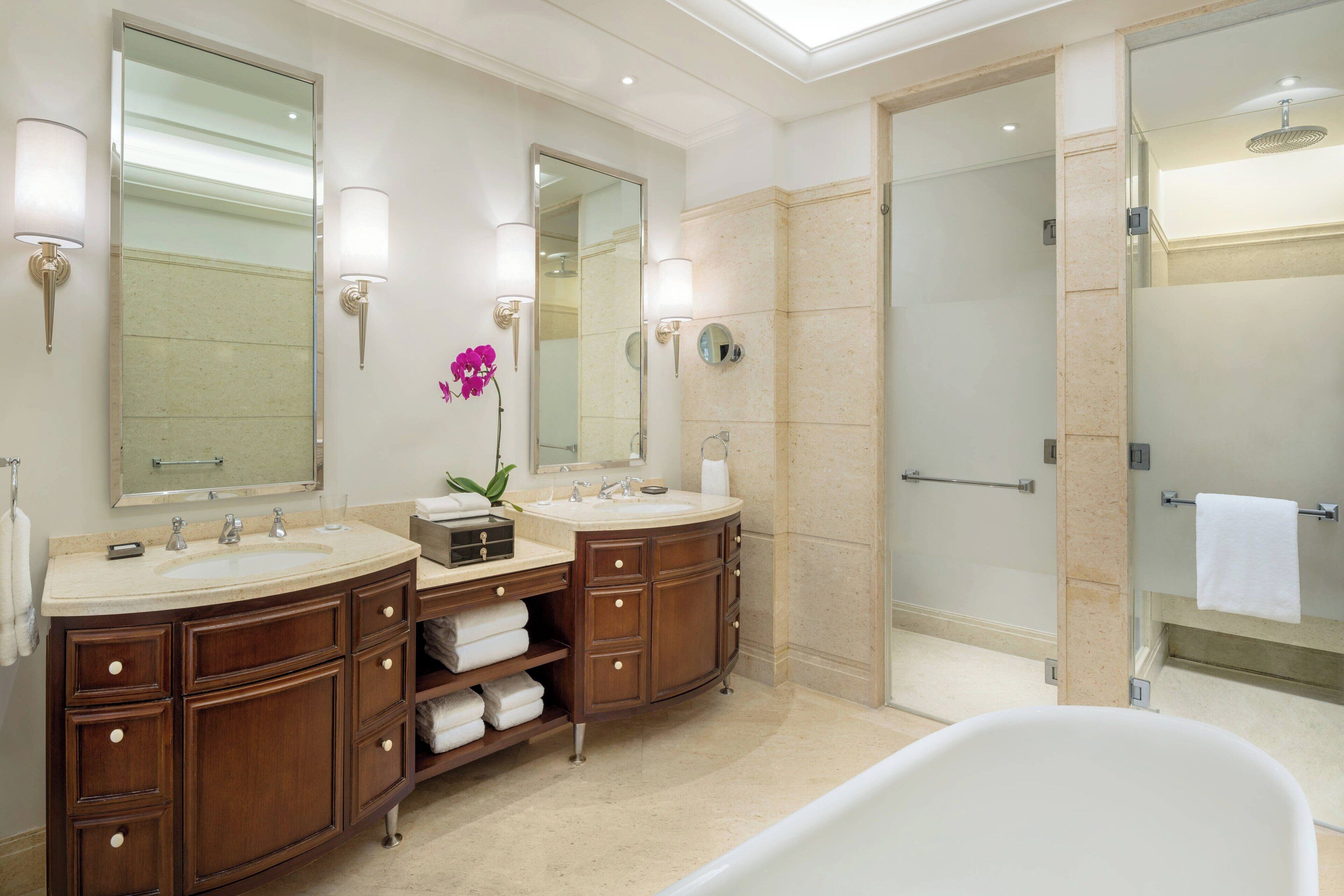 A modern bathroom with two sinks, a large mirror, and a walk-in shower.