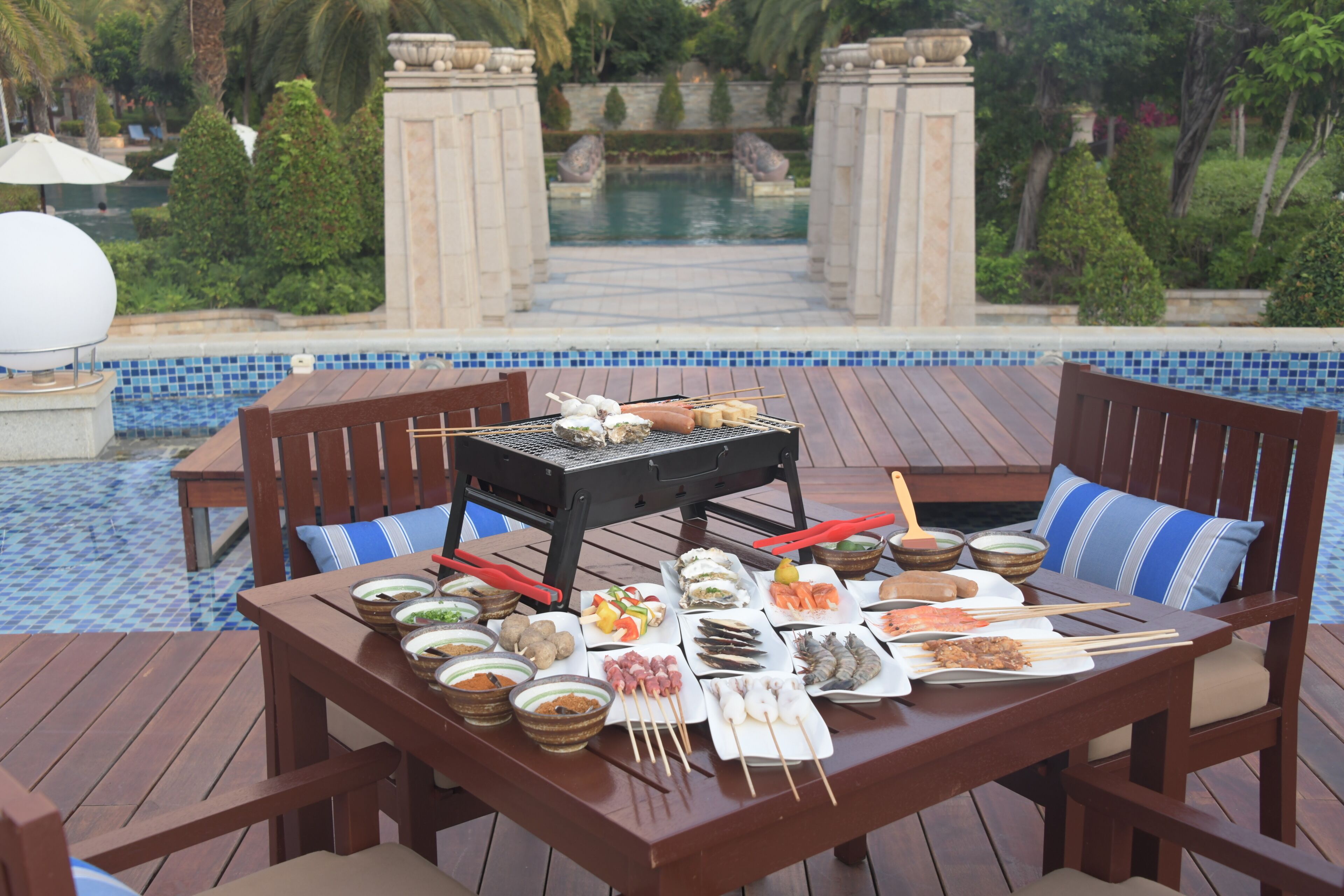 Comedor con vista a la piscina, que incluye una parrilla, diferentes platos y una mesa junto a la piscina.