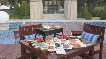 Comedor con vista a la piscina, que incluye una parrilla, diferentes platos y una mesa junto a la piscina.