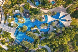 An aerial view of a resort with multiple swimming pools, palm trees, and sun umbrellas. - JW Marriott Sanya Haitang Bay Resort & Spa (Sanya)