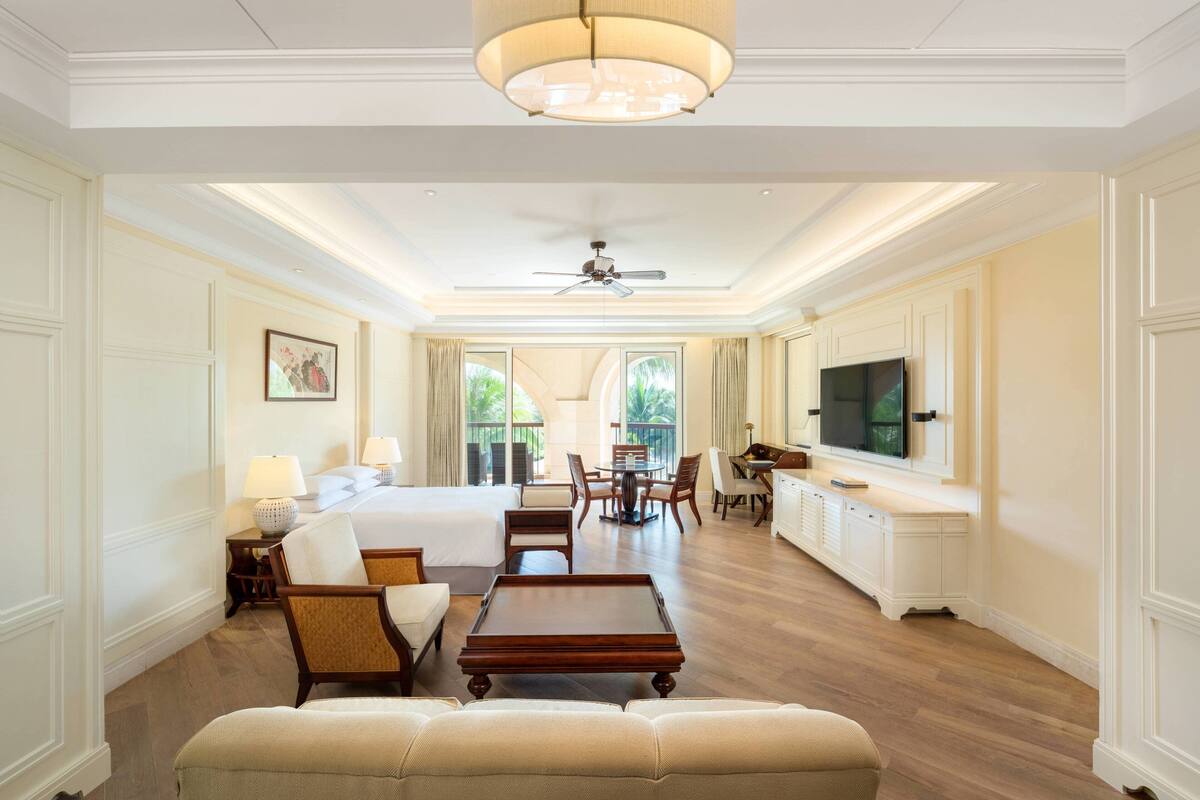 A spacious hotel room with a large bed, a sitting area with a coffee table, a dining table, and a TV.