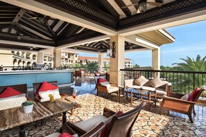 An outdoor lounge area with seating, a bar, and a view of a building with arches.