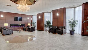 Een ruime lobby met een grote kroonluchter, leren banken, een flatscreen televisie en potplanten.