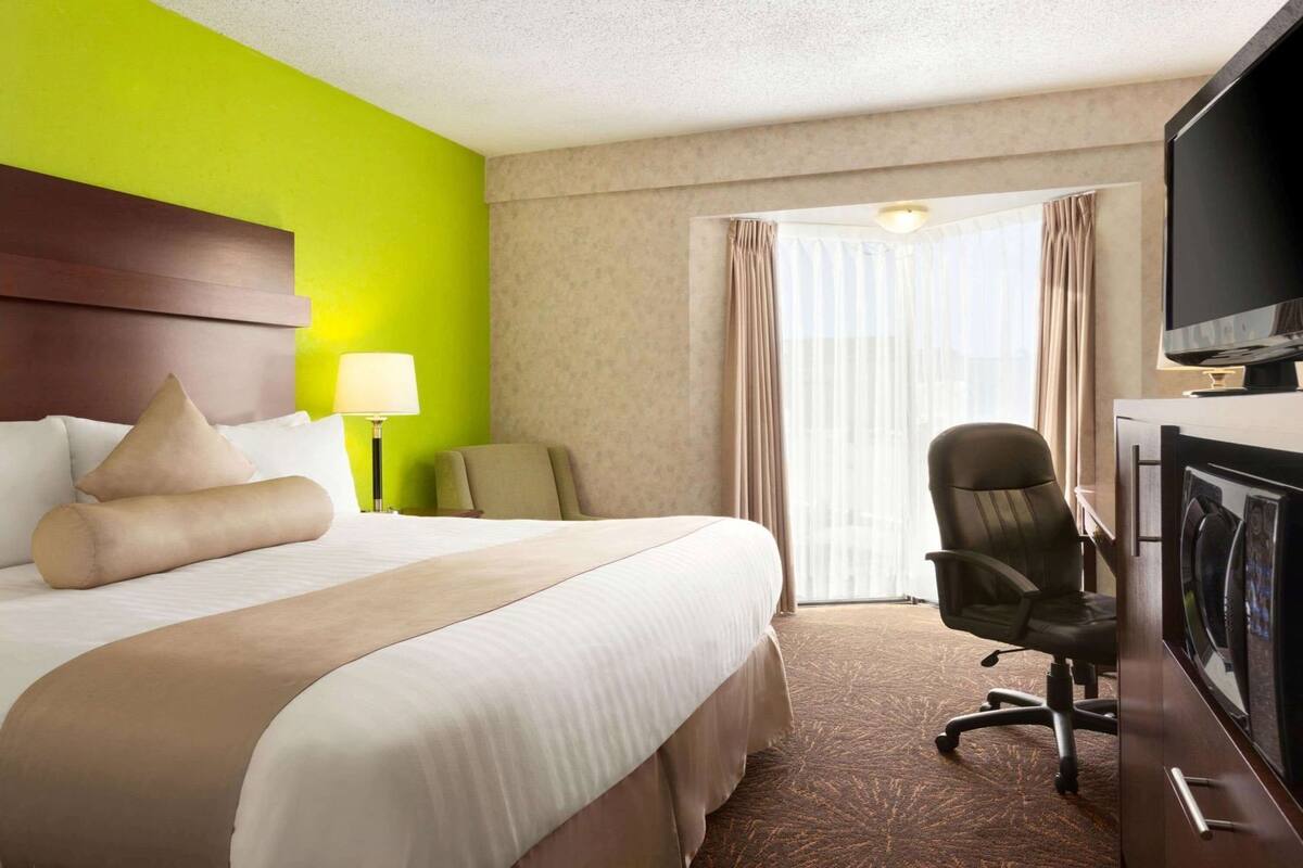 Een hotelkamer met een bed, een bureau, een stoel, een televisie en een raam met gordijnen.