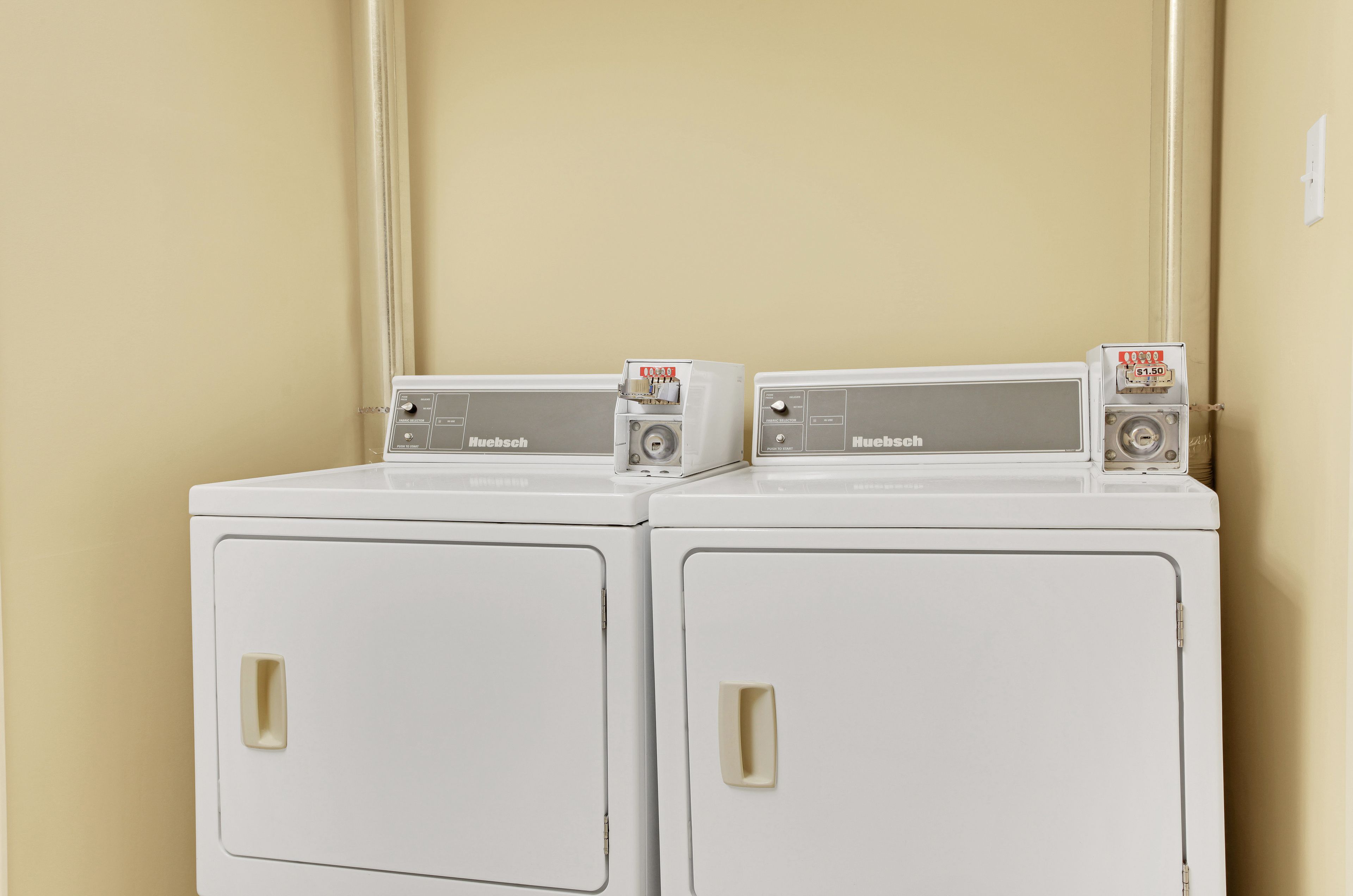 Two white Huebsch washing machines side by side against a beige wall.