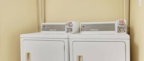 Two white Huebsch washing machines side by side against a beige wall.
