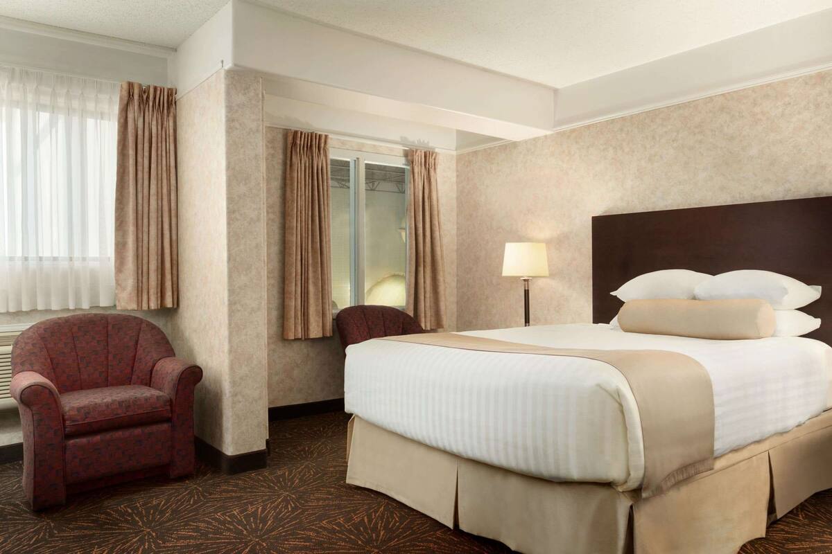 Een hotelkamer met een groot bed, een stoel, een bureau en een raam met gordijnen.