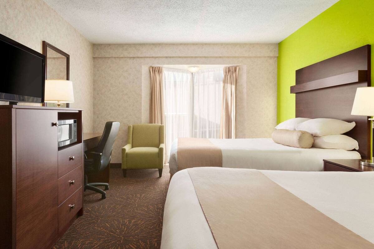 Een hotelkamer met een bed, een bureau met een televisie, een stoel en een raam met gordijnen.