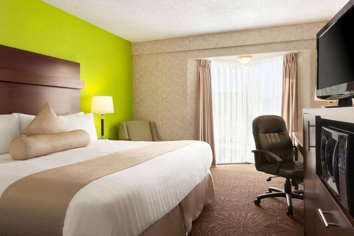 Een hotelkamer met een groot bed, een bureau met stoel, een televisie en een raam met gordijnen.