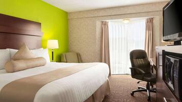 A hotel room with a large bed, a desk with a chair, a television, and a window with curtains.