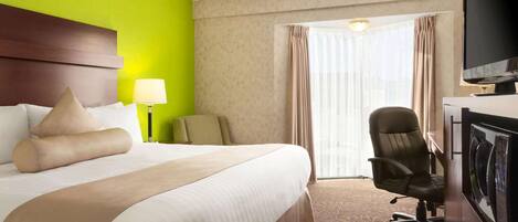 A hotel room with a large bed, a desk with a chair, a television, and a window with curtains.