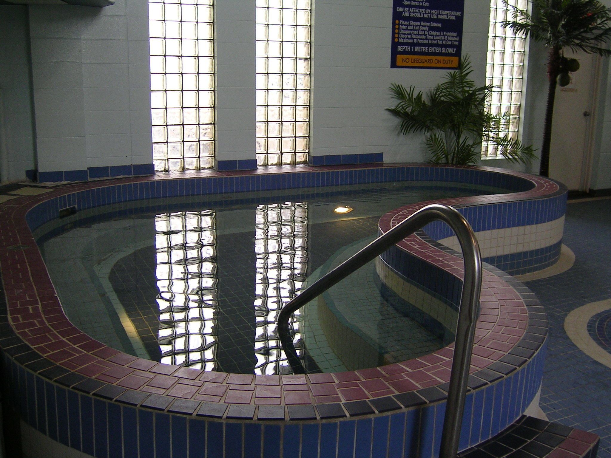 An indoor swimming pool with a tiled edge, a metal ladder, and a tiled floor.