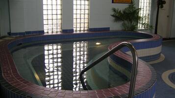An indoor swimming pool with a tiled edge, a metal ladder, and a tiled floor.