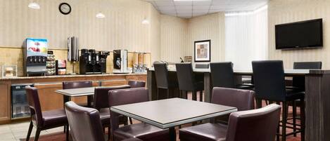 Un comedor de hotel con mesas y sillas, una máquina de café y un televisor en la pared.