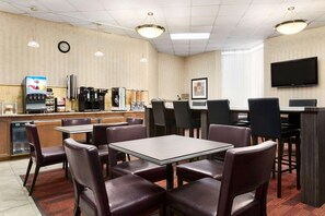 A hotel dining area with tables and chairs, a coffee machine, and a television on the wall.