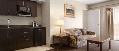A hotel room with a kitchenette, a sofa, a coffee table, and a lamp.