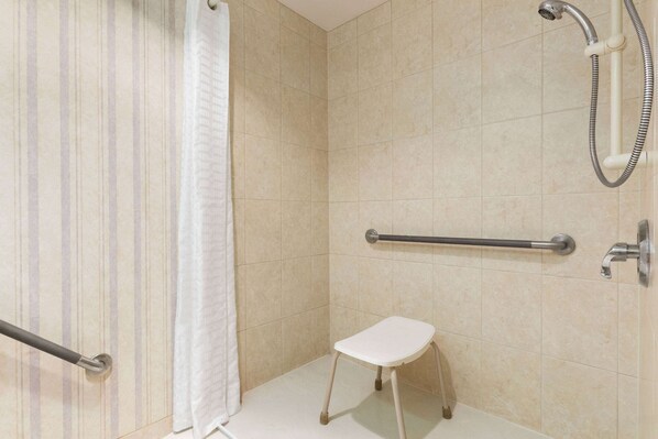 Zona de ducha con barra de apoyo, un taburete blanco y cabezal de ducha.