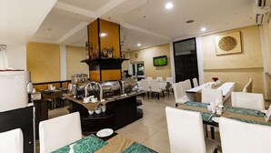 A hotel dining area with a buffet setup, multiple dining tables, and a television mounted on the wall. - Airport West Hotel (Accra)