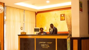 A reception desk at Airport West Hotel with a clock, a sign reading "Reception," and a decorative wall with floral patterns. - Airport West Hotel (Accra)