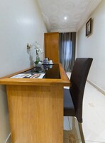 A reception desk with a wooden finish, a black chair, and a vase with white flowers.
