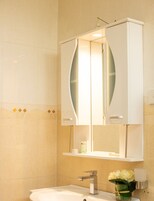 Un baño con lavamanos blanco, un mueble espejo y un florero con flores.