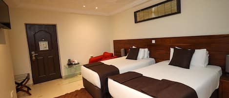 A hotel room with two beds, a wooden headboard, a brown rug, a door, and a small table with a red chair.