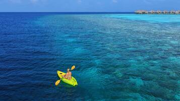A person kayaking on clear turquoise water with overwater bungalows in the background.