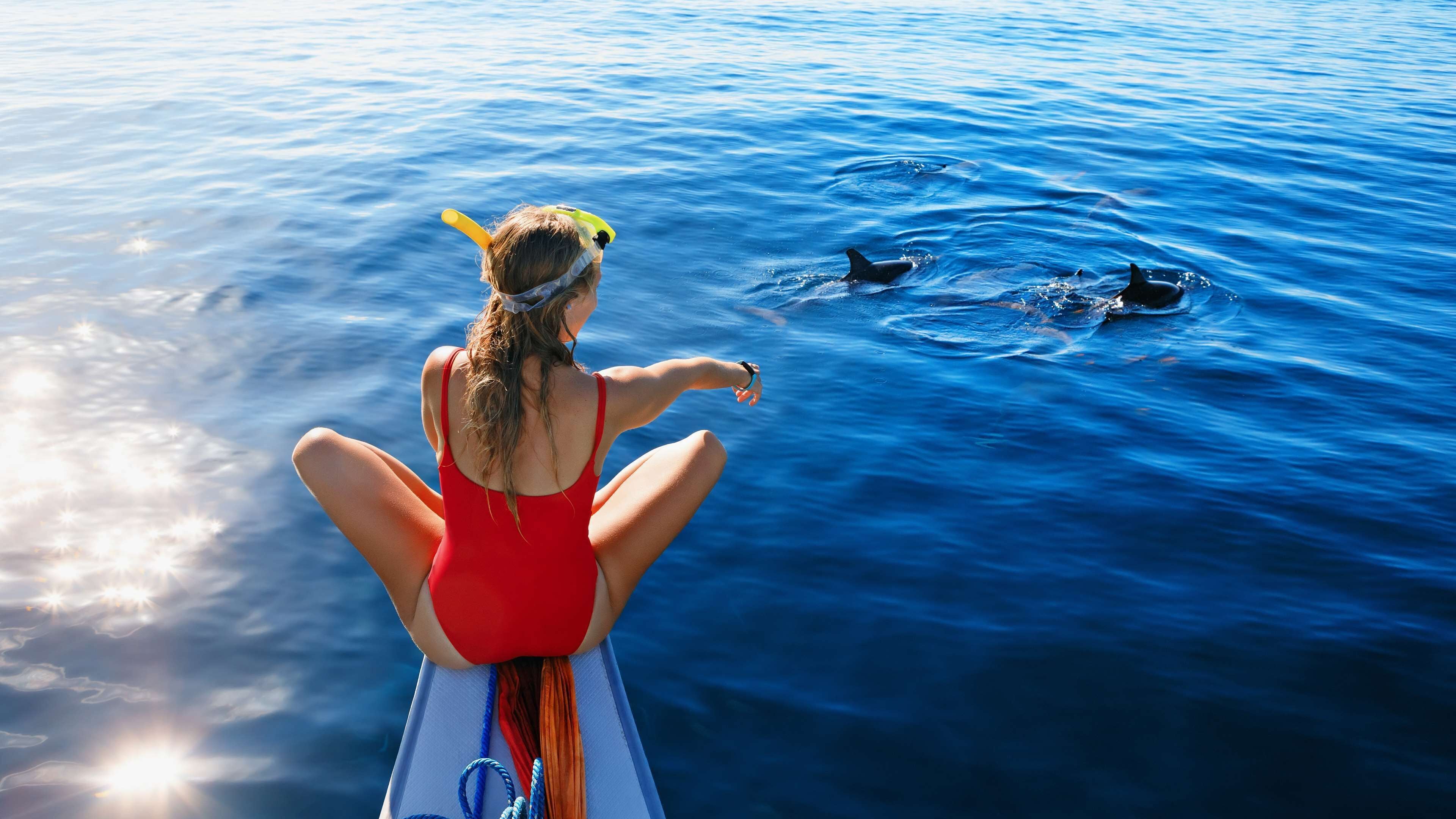 A person in a red swimsuit sitting on a boat, facing the ocean.