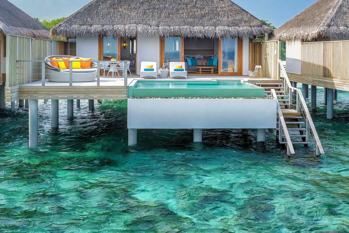 Bungalows over vandet med stråtækte tage, en pool og en træterrasse.