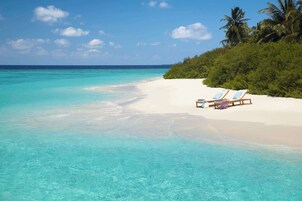 A beach with clear turquoise water, white sand, and two lounge chairs with towels.