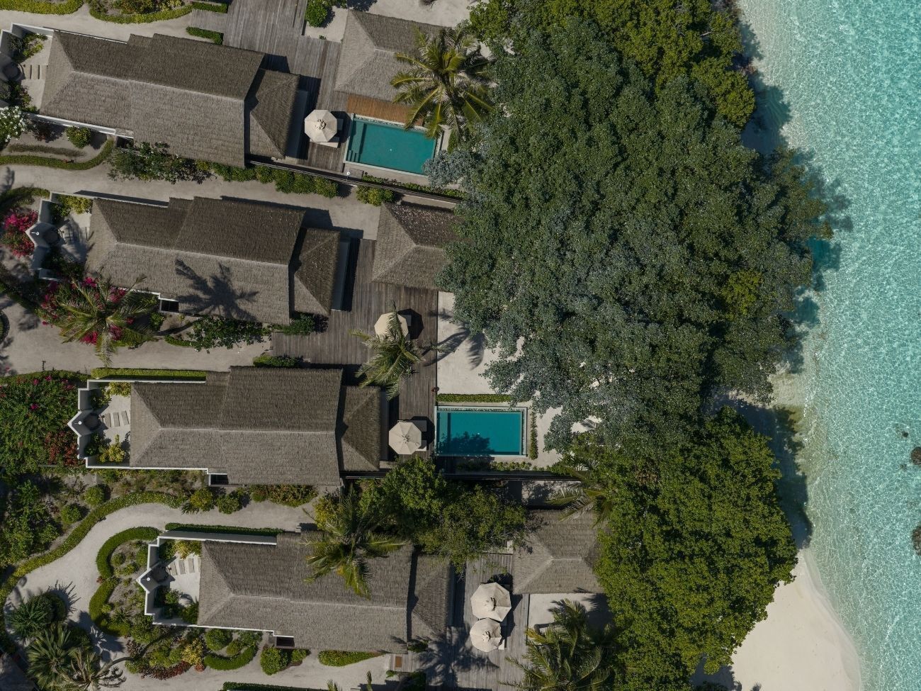 Vista aérea de un resort con varias cabañas, una piscina central y acceso a la playa.