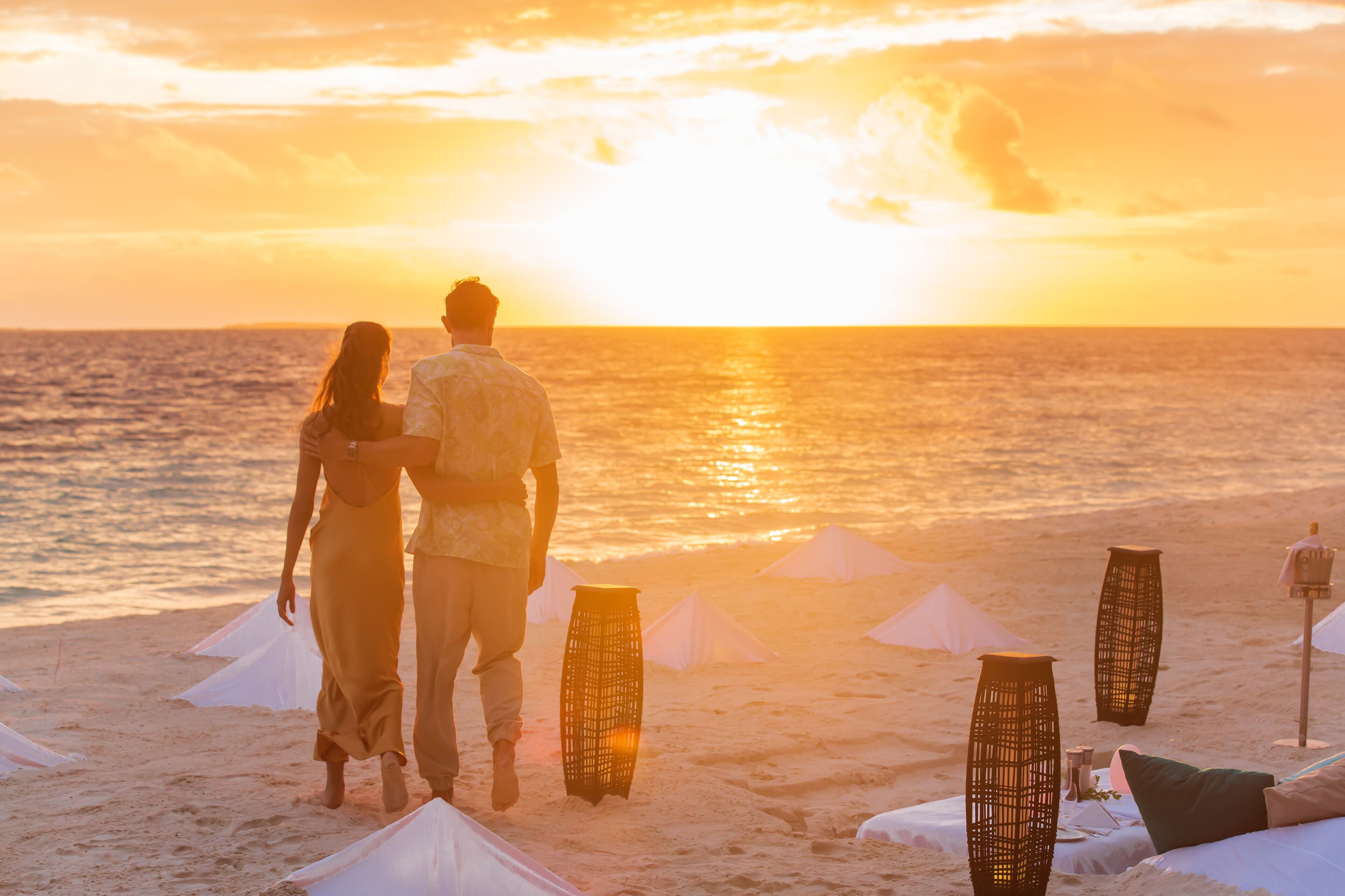 A beach scene with a sunset, white tents, and wicker tables.