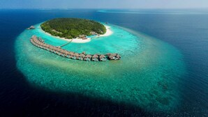 An aerial view of a tropical island resort with overwater bungalows connected by a long pier, surrounded by clear turquoise waters and a small sandy beach. - Dusit Thani Maldives - 50 percent off on Transfers for Stays of 5 Nights stay until 20 December 2026 (Mudhdhoo)