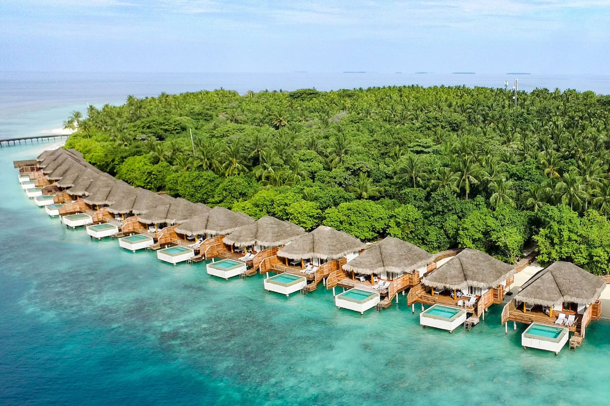 An overwater bungalows with thatched roofs and private pools, surrounded by lush greenery and clear turquoise waters.