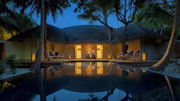 Un resort con piscina, edificaciones de techo de paja y palmeras.