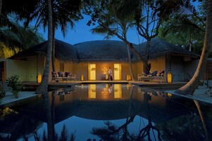 Un resort con piscina, edificaciones de techo de paja y palmeras.