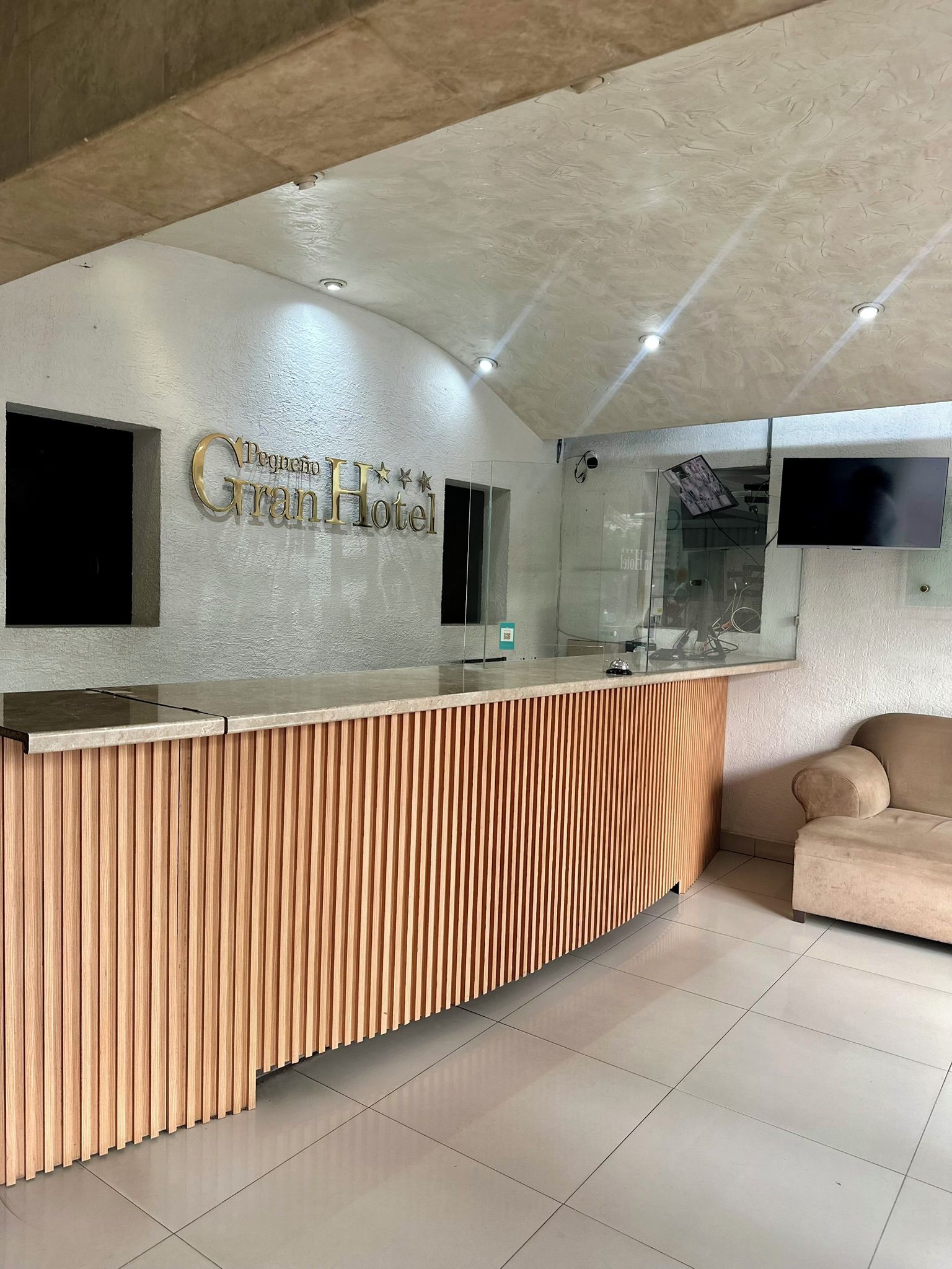 A reception desk with a wooden panel design, a flat-screen TV mounted on the wall, and a sofa in the background.