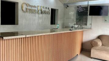 A reception desk with a wooden panel design, a flat-screen TV mounted on the wall, and a sofa in the background.
