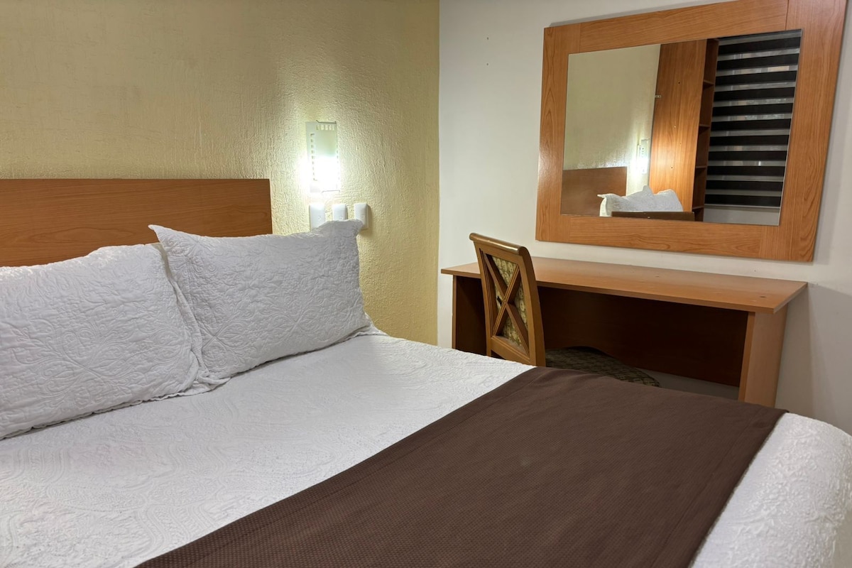 Una habitación de hotel con una cama, un escritorio y un espejo.