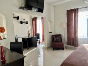 A hotel room with a bed, a desk, a chair, a TV, and a floor lamp. - Pequeno Gran Hotel (Aguascalientes)